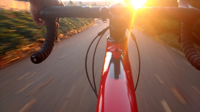 Photo taken behind a bicycle's handlebars as it's being ridden towards a sunset