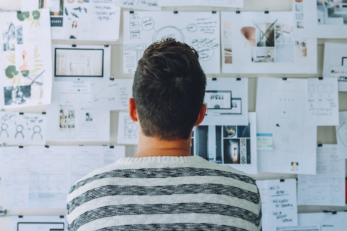 Man looking at wall with printouts of graphics and charts pinned to it 